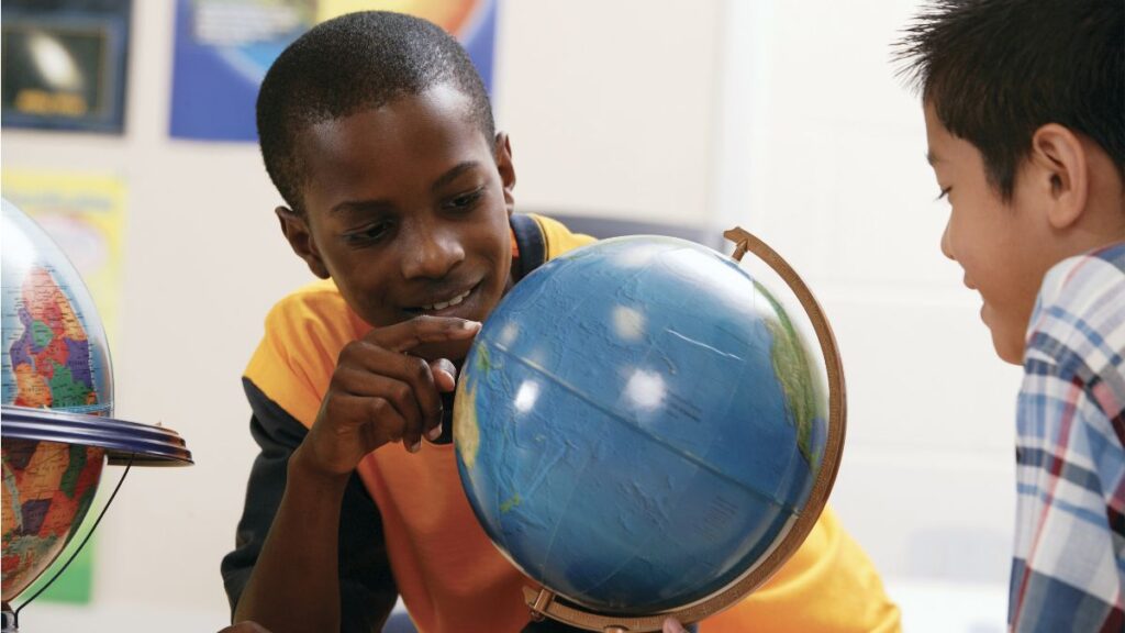 A young student holding a classroom globe while learning about geography and world cultures in a social studies lesson.