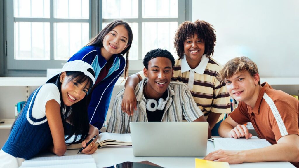Happy students working together on a laptop using study tools to manage university assignments.
